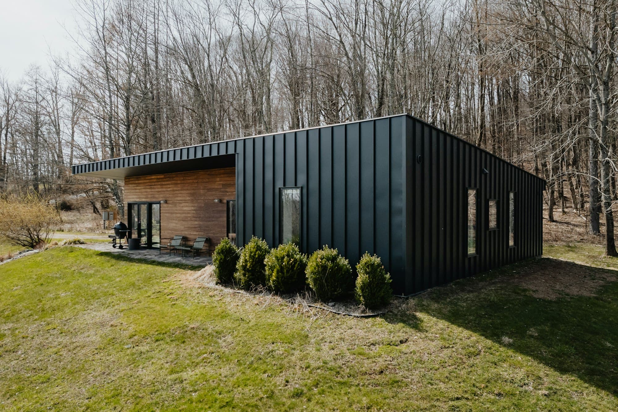 A long, low black-clad building on a lawn with a row of clipped shrubs