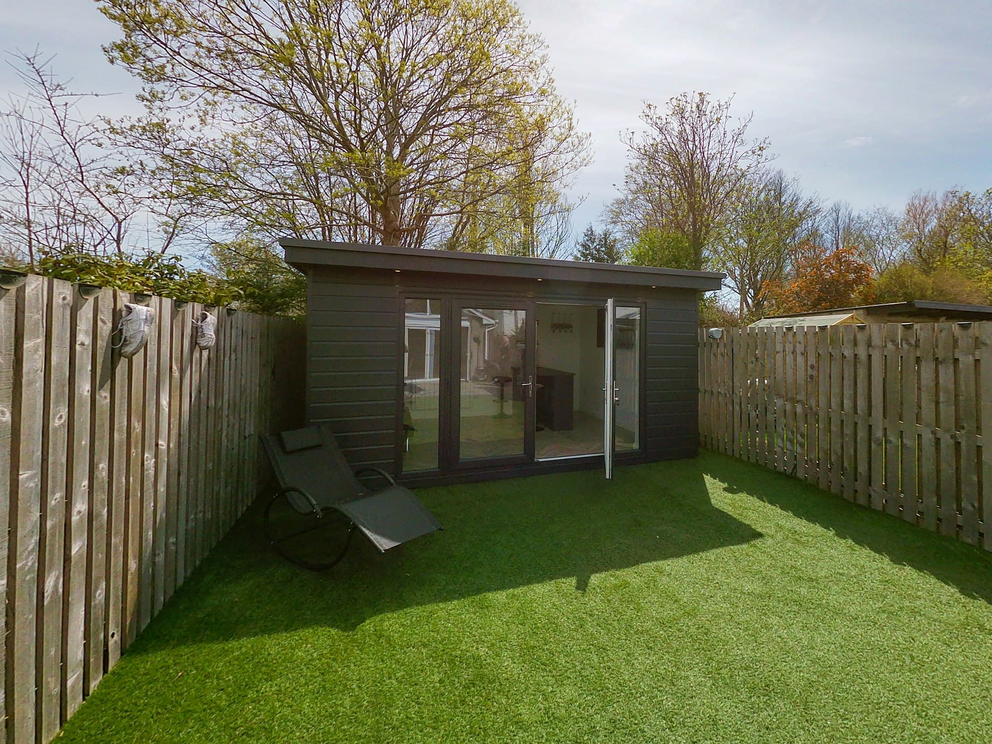 A compact dark-clad garden office at the end of a lawn